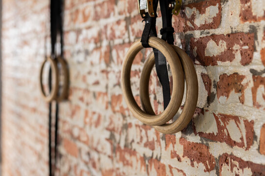 Wooden gymnastic rings hanging from black straps on exposed brick wall inside fitness studio