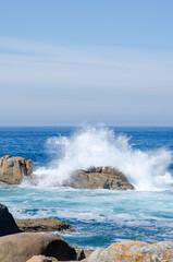 Dramatic ocean waves collide with rugged rocks on a sunny day, creating powerful splashes and a sense of natural energy at the coastline. Perfect for nature themes.