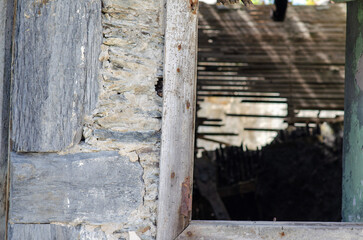 Close-up of a weathered stone wall and rustic wooden window frame in an abandoned building, capturing historic rural architecture and a sense of decay.