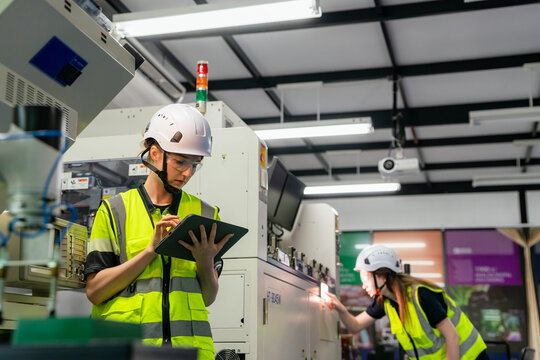 A man in a yellow vest is looking at a tablet. Female engineer working with automated machinery in a smart factory, concept of Industry 4.0 and manufacturing technology.