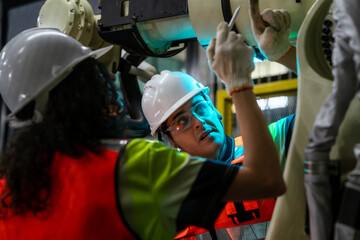 Two people wearing safety gear are working on a machine. Team of engineers collaborating on programming and maintenance of a robotic arm in a smart factory.
