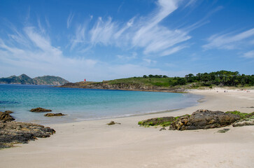 Tranquil sandy beach with turquoise sea, rocky coast, and lush greenery on a bright summer day....