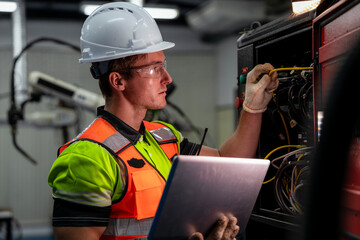 A man in a green and orange vest is working on a laptop. Electrical engineer or technician using a...