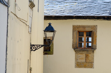 Charming close-up of an old stone window with wooden frame and classic black lantern on a rustic European house, evoking timeless village architecture.
