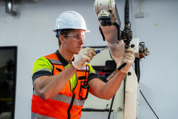 A man in a yellow and orange vest is working on a machine. Robotics engineer performing maintenance...
