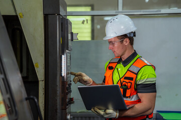 A man wearing a safety vest and a hard hat is looking at a laptop. Machinist or CNC machine...