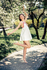 Graceful young woman enjoying blooming park in white summer dress under spring sunshine