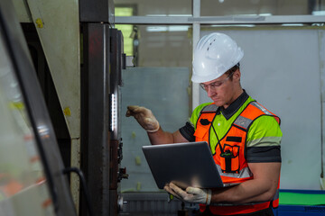 A man in a safety vest is looking at a laptop. Machinist or CNC machine operator setting up a cutting tool for a milling machine in a metalworking factory.