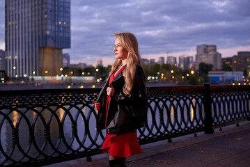 A woman in a red dress goes along the embankment. It has a black jacket. The action takes place at...