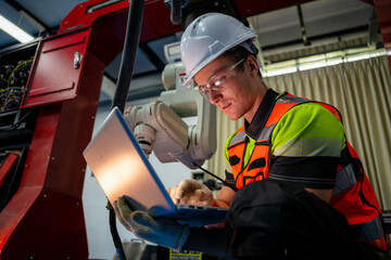 A man in a yellow and green vest is sitting on the floor and looking at a laptop. Concept of Industry 4.0 with diverse engineers collaborating on automation technology.