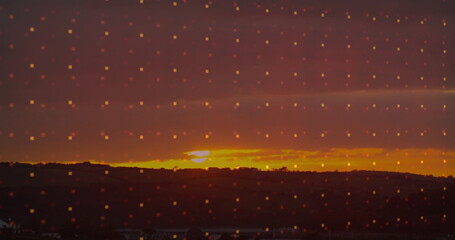 Displaying vivid sunset casting orange glow over rural hills, low clouds at dusk, with pixelation