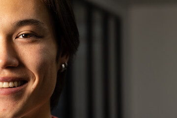 Asian man smiling half-face in side-lit room showing silver hoop earring against bars, copy space