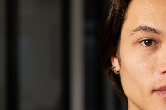 Asian man showcasing small hoop earring close up in room with blinds background, copy space