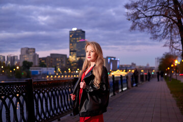 A woman in a red dress goes along the embankment. It has a black jacket. The action takes place at...