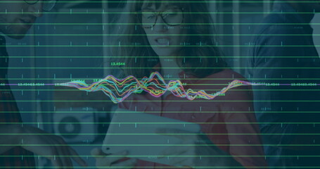 Collaborating team analyzing data on tablet in office, with green data line graphs and waveforms