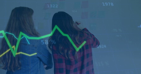 Two colleagues marking sticky notes and referencing graph in conference room, with markers