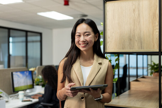 Diverse coworkers wearing business attire holding tablet and typing on computer in open-plan office - Powered by Adobe