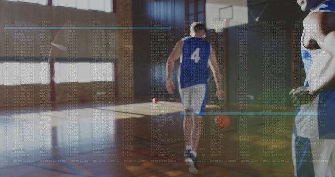 Walking basketball player wearing blue and white jersey toward hoop in school gym, with basketballs