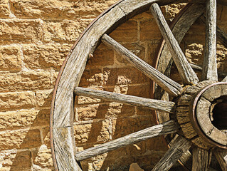 Weathered Wagon Wheel Resting Against a Textured Stone Wall Under Sunlight, Western Style