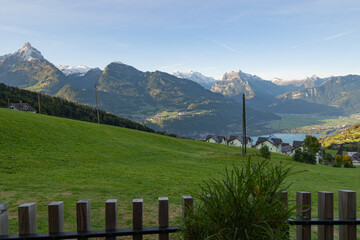 Expansive View of a Swiss Alpine Valley with Green Pastures, Lake, and Mountains