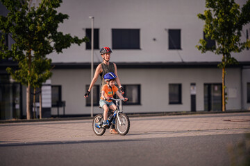 Fototapeta premium Adult Teaching Young Child to Ride Bicycle on City Street