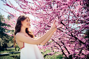 Lovely woman in white dress enjoying springtime near blossoming flowers outdoors in sunny park