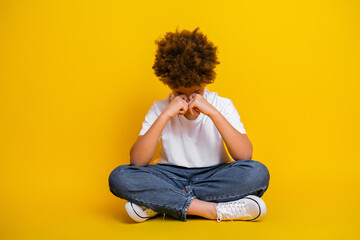 Young boy in casual outfit sitting with thoughtful gesture on yellow background reflecting emotions and youthfulness