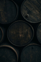 Wooden barrels stacked closely together, a pattern of dark wood and metal bands. Industrial storage and aging process for wine or whiskey background.
