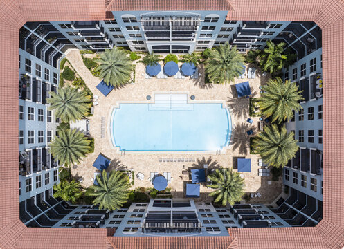 Aerial view of a symmetrical courtyard with a gleaming pool reflecting the sky, framed by palm trees and building architecture, Fontainebleau, Florida, United States.