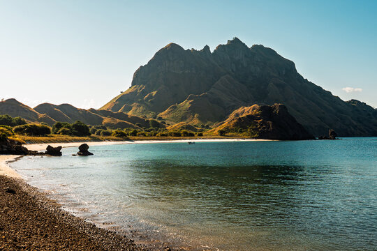 Peaceful turquoise bay with dramatic green hills and rocky coastline under clear sky