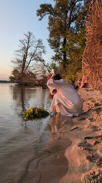 Ukrainian girl in wreath poses near water.
