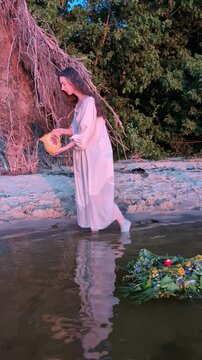 Ukrainian girl in wreath poses near water.
