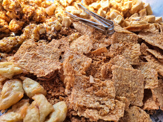 Close-up of assorted Indonesian deep-fried snacks or gorengan, including crispy tempeh crackers and tofu, displayed in a street food stall