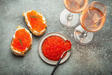 Small metal plate with red salmon caviar, two caviar toasts canape, two glasses of champagne top...