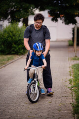 Parent Teaching Young Child to Ride Bike on Sidewalk