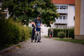 Parent Teaching Young Child to Ride Bike on Sidewalk