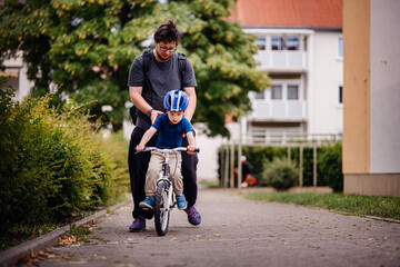 Parent Teaching Young Child to Ride Bike on Sidewalk
