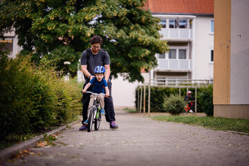 Parent Teaching Young Child to Ride Bike on Sidewalk