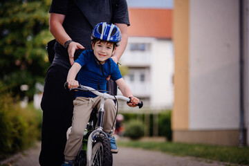 Parent Teaching Young Child to Ride Bike on Sidewalk
