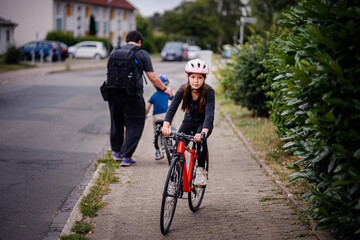 Girl Cycling on Sidewalk as Sibling Learns to Ride Nearby