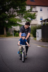 Parent Teaching Young Child to Ride Bike on Sidewalk