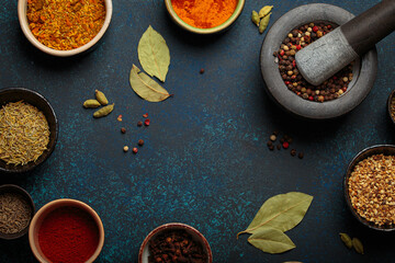 Colorful bowls of aromatic spices and herbs on a dark background, with a mortar and pestle,...