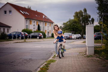 Woman Helping Young Boy Learn to Ride Bike on Sidewalk