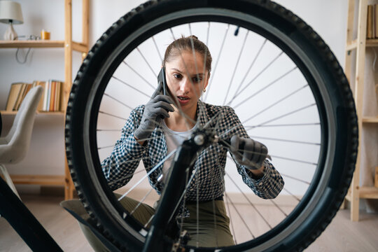 Young woman talking on mobile phone with mechanic asking for advice on servicing repairing broken bicycle