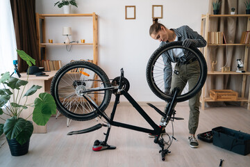 Female cyclist secure wheel on bicycle at home. Technician holding bike parts, fixing on camera