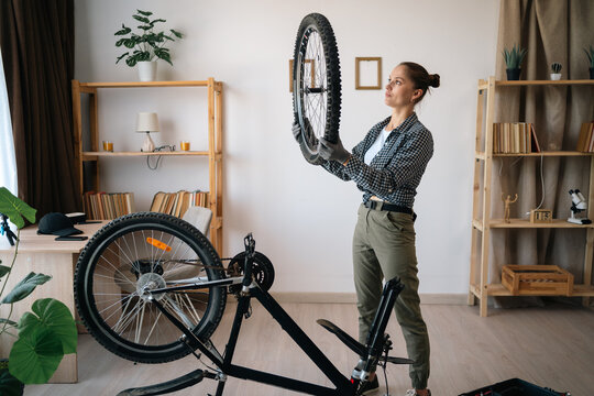 Young woman repairing her bicycle in the living room at home