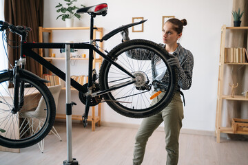 woman repairing bicycle at home by herself in living room fixing wheel fender, using tools for...