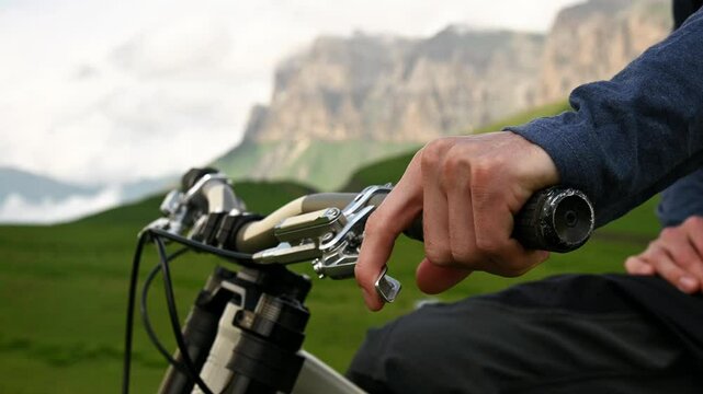 Mountain MTB bike handlebars against the backdrop of epic mountains in the clouds in defocus. Male rider puts his hand on the bicycle handlebar