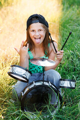 Cheerful little girl with drums. Emotional portrait of happy little girl shows her tongue and...