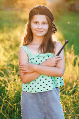 Happy little girl crossed arms smiling at camera outdoors. Portrait of adorable preschool caucasian kid 8-9 years old smiling standing in park over blurred background at sunset. Girl playing drums.